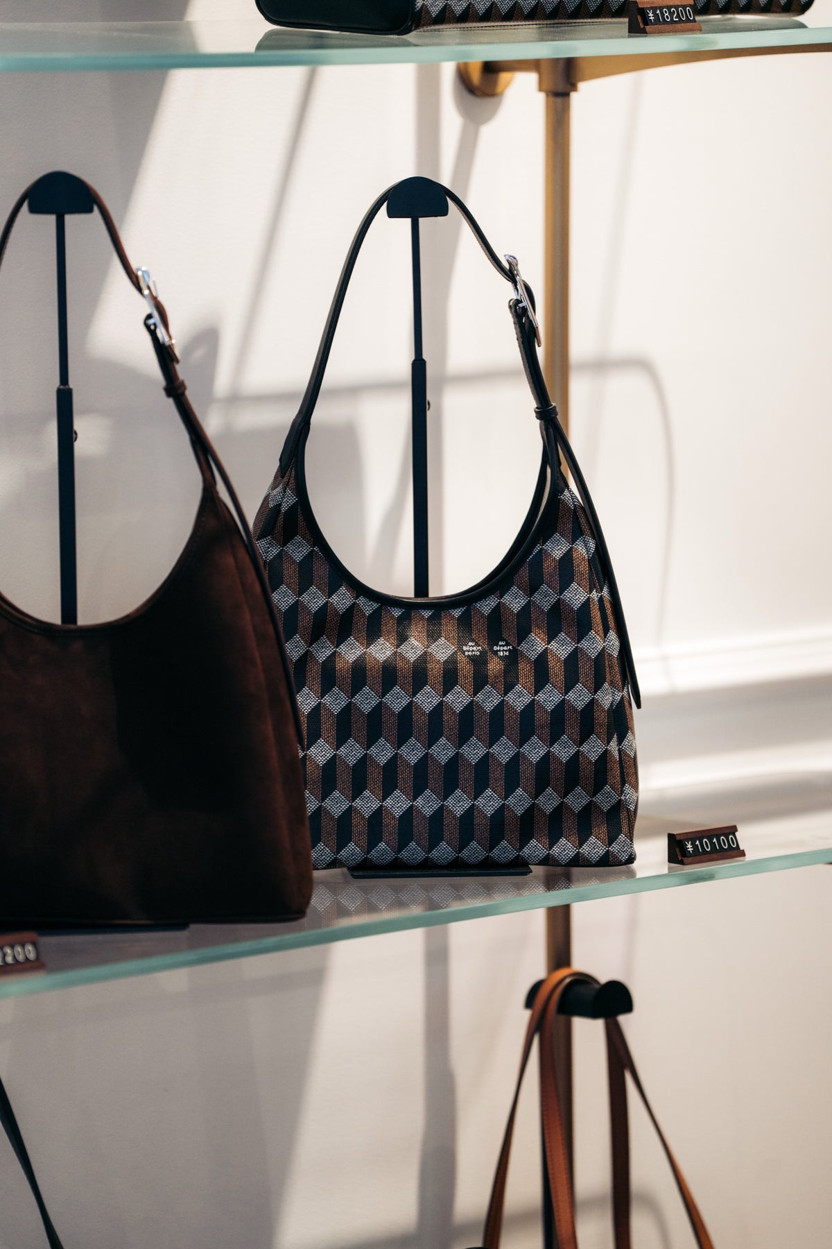 Au Départ shoulder bags on a glass display shelf